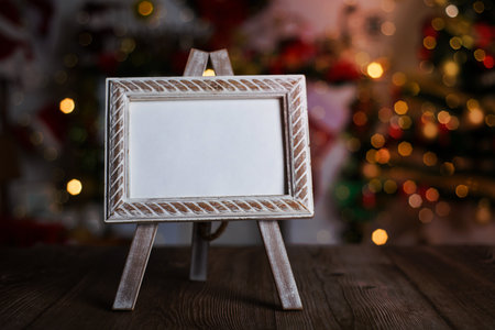Small easel with framed blank postcard on wooden table with Christmas background. Mockup of Christmas card.の写真素材