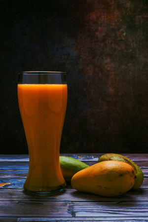 Tall glass with mango juice and mangoes on wooden table. Lateral view.の写真素材