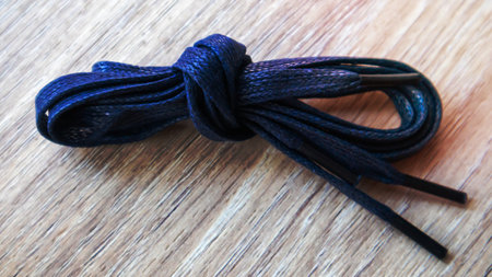A subject shot of dark blue flat laces with thin tips for shoes rolled up and isolated on a wooden background. Stylish accessoryの写真素材