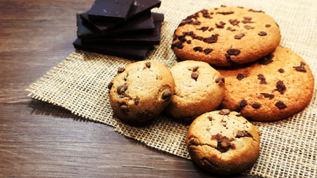 American chocolate chip cookies on a brown wooden table and on a linen napkin close-up. Traditional...