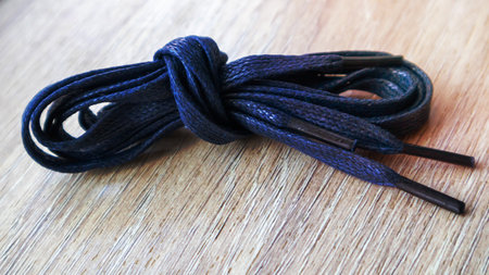 A subject shot of dark blue flat laces with thin tips for shoes rolled up and isolated on a wooden background. Stylish accessoryの写真素材