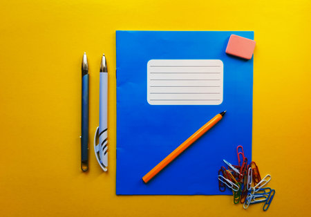 Blue mock up notebook and textbook butt for school subjects, eraser, pencil, paper clip on a yellow background. Flat lay, copy space, top view, place for textの写真素材