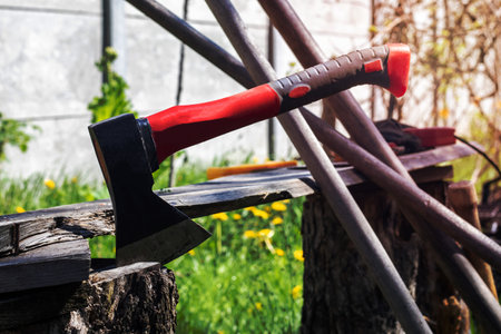 An ax with a red handle plunges into a stump. Sawmill operation concept. Woodworking. Stump and ax in sunny weather. Preparing firewood for the winter. Selective focus, blurred backgroundの写真素材