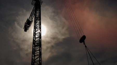 Construction crane on a background of blue sky. Close view of a construction crane. Abstract industrial background with a silhouette of a construction crane over the sky with cloudsの写真素材
