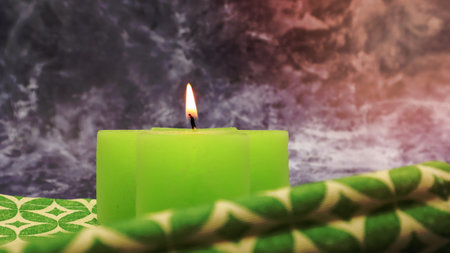 Composition with one green lit candle on a table with a green linen napkin against a beautiful gray marble background. Place for your text. Christmas decorationsの写真素材
