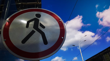 A round road sign of white and red with a black man in the center, prohibiting the movement of pedestrians on a background of blue sky and white clouds. No pedestrians allowed at this place.の写真素材