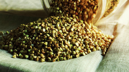 Green raw buckwheat is poured out of a glass jar on the table. Buckwheat grain. Agriculture. Healthy and vegetarian food on the table. Cook at home. Safe, environmentally friendly and healthy productの写真素材