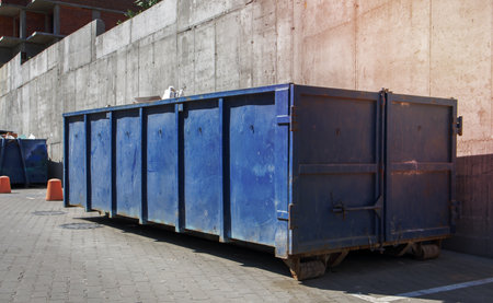 Metal durable blue industrial trash bin for outdoor trash at construction site. Large waste basket for household or industrial waste. A pile of wasteの写真素材