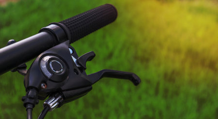Mountain bike steering wheel on green grass background. Details of sporting events. Close up black mountain bike knob and derailleur knob, left shifterの写真素材