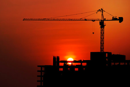 Silhouetted construction crane and building at construction site on sunset for construction industrial work conceptの写真素材