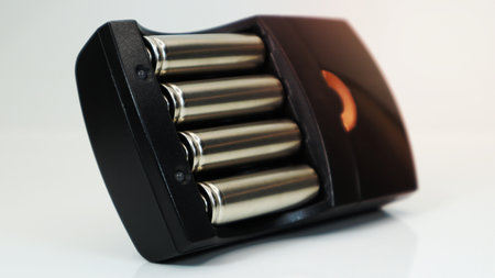 Rechargeable alkaline batteries in a battery charger on a white background. AA fast charger in black. The battery is chargingの写真素材