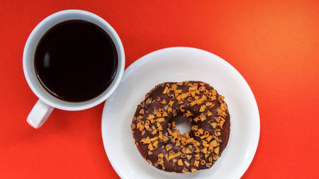 One chocolate donut and black Americano coffee without milk in a white cup on a bright background. Top view, flat lay. Fresh brewed or instant hot coffee drink. Monochrome conceptの写真素材