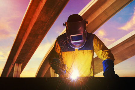 Industrial Worker with safety equipments and protective mask welding steel structure with expressway the infrastructure for transportation in background. Elegant design for construction conceptの写真素材