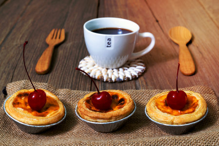 egg tart in aluminum foil cup with red cherry and coffee on wood tableの写真素材