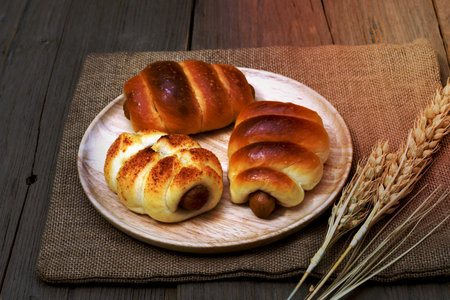 Sausage bread and wheat ears and sack on wooden background.の写真素材