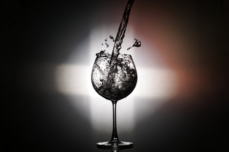 Pouring water in to the wine glass with rear light on black backgroundの写真素材
