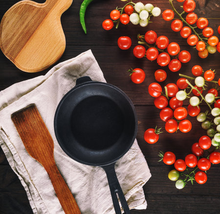 empty cast iron round frying pan and ripe red cherry tomatoes on a brown wooden table, top viewの写真素材