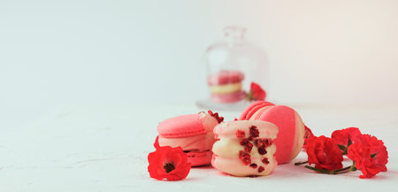 baked red strawberry macarons and rosebuds on a white table, gourmet almond flour dessert, close upの写真素材