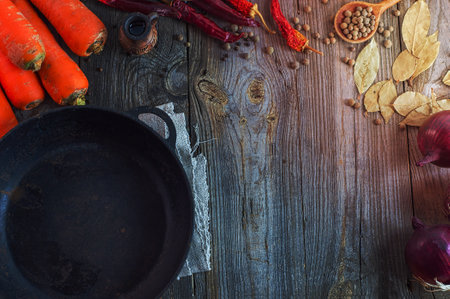black cast iron pan with carrots and onions on a gray wooden surface, empty space in the middleの写真素材