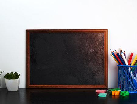 empty black chalk board, multi-colored pencils in a blue metal stand on a black table, concept back to schoolの写真素材