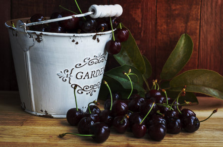 Fresh dark red cherries in a bucket on a wooden tableの写真素材