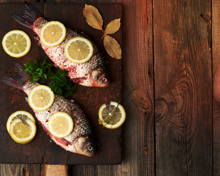 fresh crucian fish sprinkled with spices and lemon slices and lies on a brown wooden cutting board, wooden table from boards, top viewの写真素材