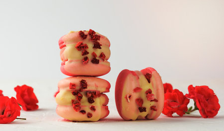 baked red strawberry macarons and rosebuds on a white table, gourmet almond flour dessert, close upの写真素材