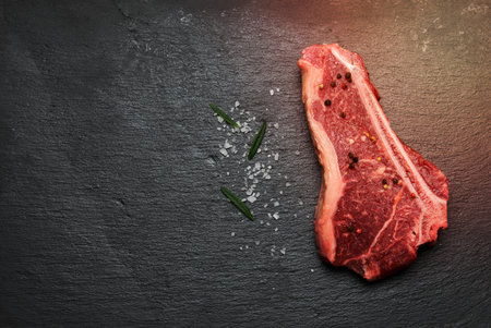 fresh raw piece of beef meat, striploin steak lies on a black board with spices, top viewの写真素材