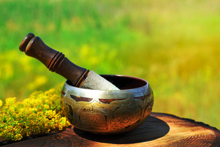 Copper singing bowl with a stick on a wooden table, blurred background of natureの写真素材