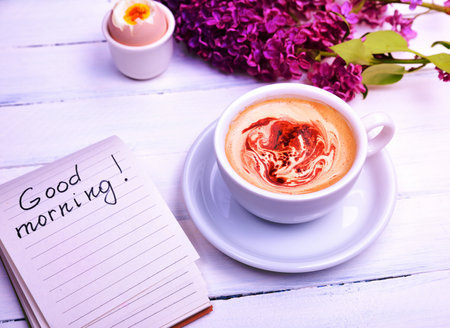 Cappuccino in a white cup, next note with the inscription good morning, white wooden tableの写真素材