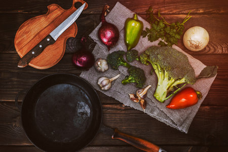 empty black cast-iron frying pan and fresh vegetables on a brownish wooden table, top viewの写真素材