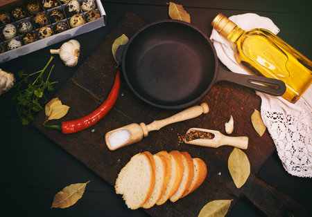raw quail eggs and an empty round black cast-iron frying pan on a brown wooden board, next to a glass bottle with oil, top viewの写真素材