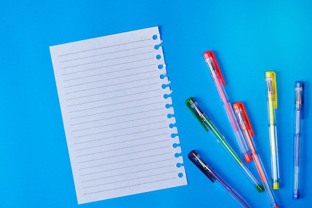 empty paper sheet in a line and multi-colored gel pens on a blue backgroundの写真素材