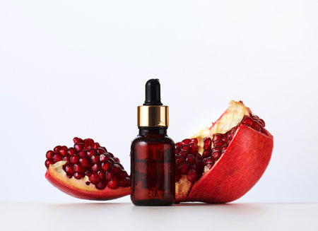 brown glass bottle with a pipette and red pomegranate seeds on a white background. Template for cosmetic liquid products, advertising and promotionの写真素材