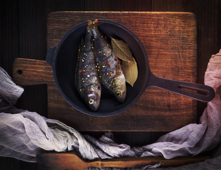 fresh peeled fish from scales with spices in a round black cast-iron frying pan, top viewの写真素材
