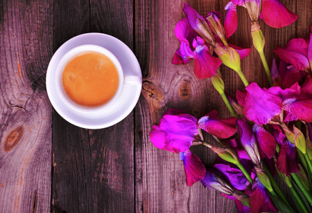 Cup of coffee and a bouquet of purple irises on a gray wooden surface, top viewの写真素材