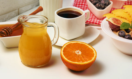 half a ripe orange and freshly squeezed juice in a glass transparent decanter, a cup of coffee, honey and oatmeal on a white table. Morning breakfastの写真素材