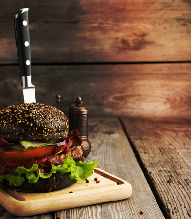 cheeseburger with black bun, meat and vegetables on a wooden background, fast foodの写真素材