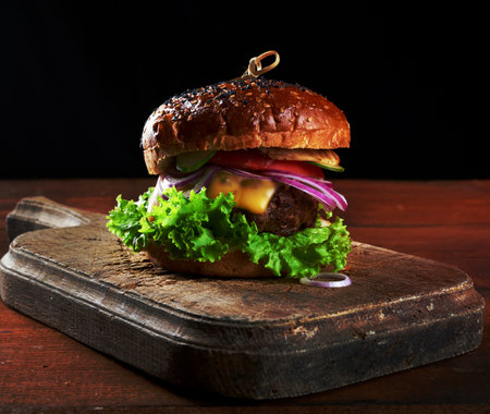 delicious burgers with fried beef cutlet, tomato, lettuce and onions, crispy white wheat flour bun with sesame seeds. Fast food on a wooden board, top viewの写真素材