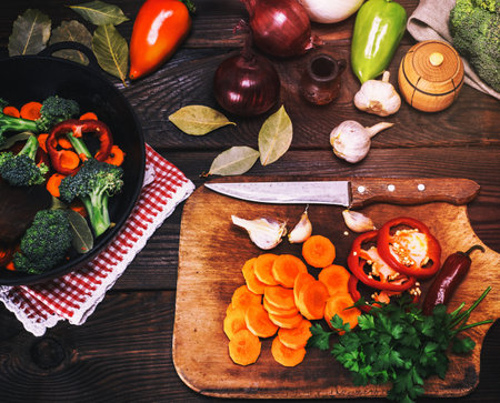fresh pieces of broccoli, carrots and red peppers in a black cast-iron frying pan on a brown table, top viewの写真素材
