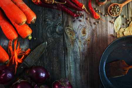 Fresh carrots and red onion with a frying pan on a gray wooden surface, top view, an empty space in the middleの写真素材