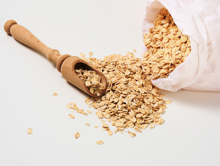 raw oatmeal in a white paper bag and a wooden spoon on a white table, breakfast porridgeの写真素材