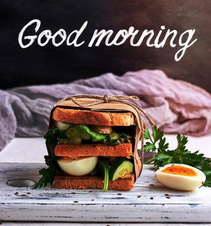 sandwich of French toast and lettuce leaves and boiled egg, a vegetarian food wrapped in paper, inscription good morning white chalkの写真素材