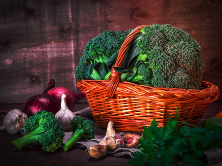 fresh broccoli in a brown wicker basket and garlic with onion on a wooden tableの写真素材