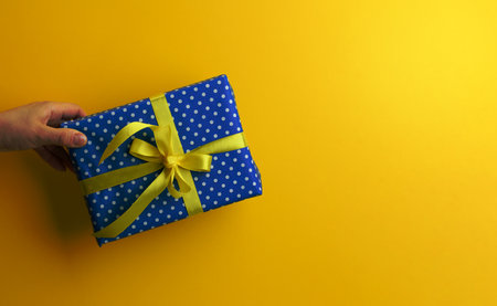 female hand are holding a blue gift box on a yellow background, happy birthday concept, copy spaceの写真素材
