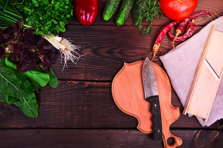 fresh vegetables and herbs for salad with a wooden cutting board and knife on a brown wooden background, top viewの写真素材