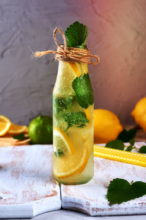 summer refreshing drink lemonade with lemons, mint leaves, lime in a glass bottle, next to the ingredients for making a cocktailの写真素材