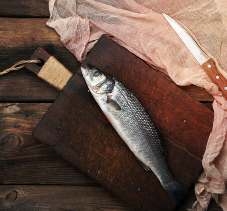 fresh whole sea bass fish on brown cutting board , top viewの写真素材