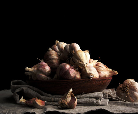 raw unpeeled garlic in a brown ceramic plate on a gray linen napkin, dark backgroundの写真素材