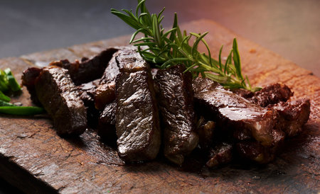 roasted piece of beef ribeye cut into pieces on a vintage brown chopping board, rare doneness. Appetizing steakの写真素材
